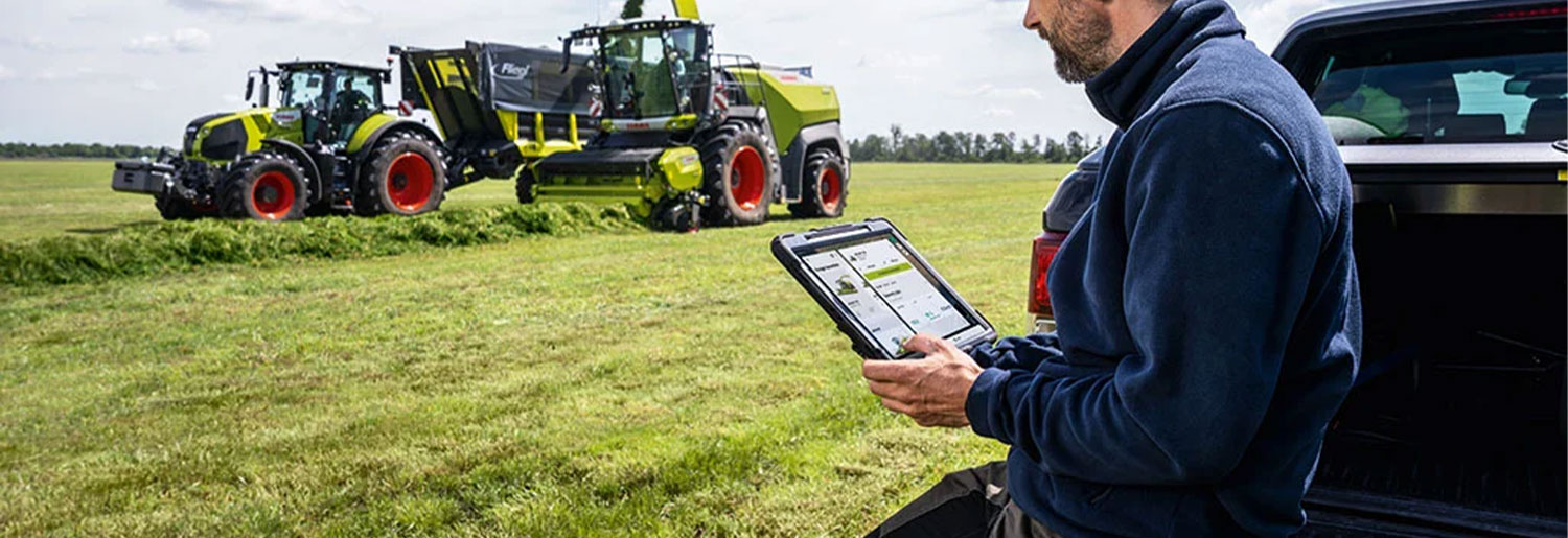 Driver using a tablet beside a CLAAS tractor in a field